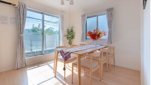 A bright, sunlit dining area with a wooden table and chairs, large windows, and a ceiling light fixture. - Popular Shinjuku area Maximum12 People (Tokyo)