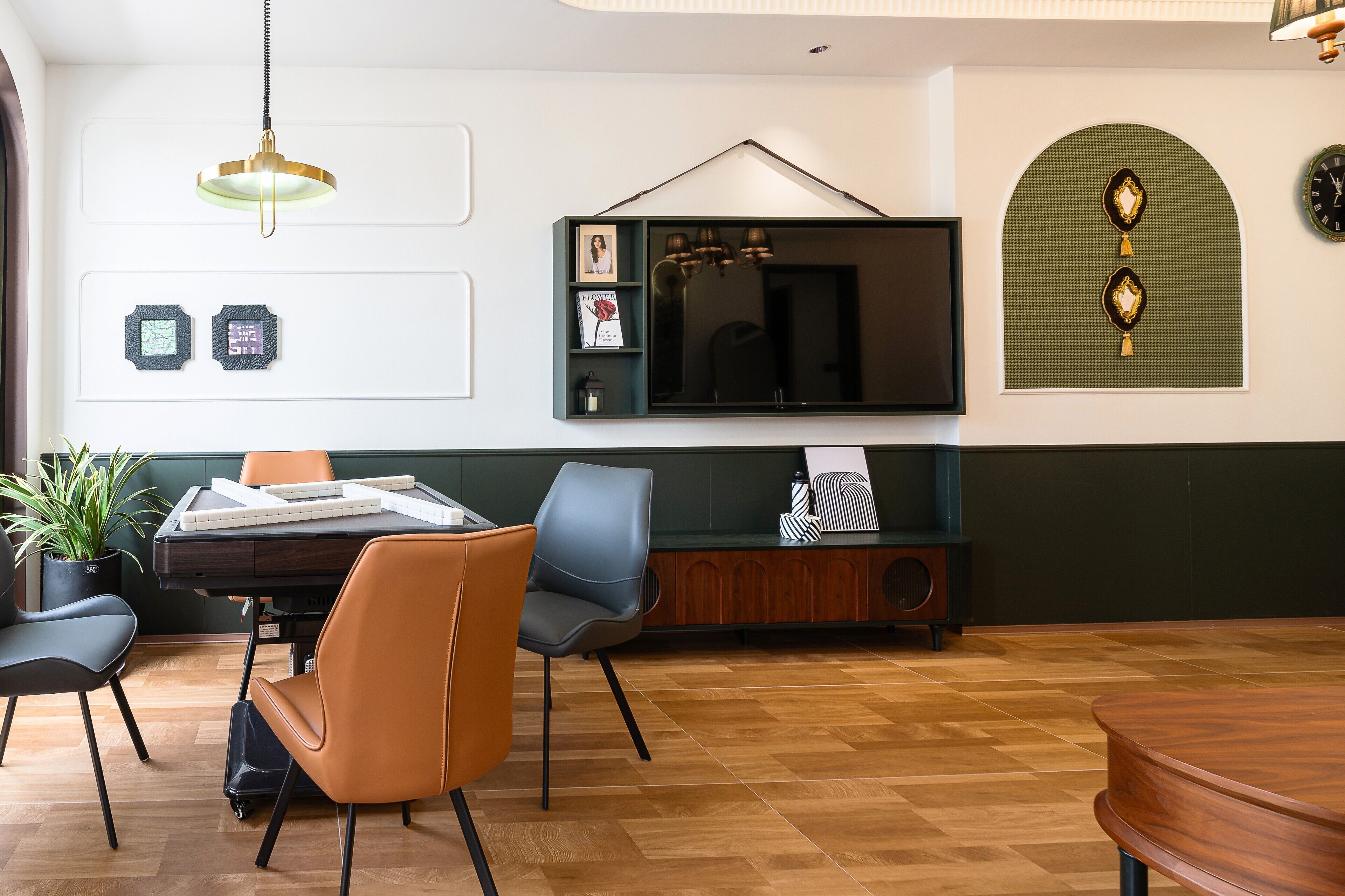A modern dining area with a wooden table, two chairs, a potted plant, and a television mounted on the wall.