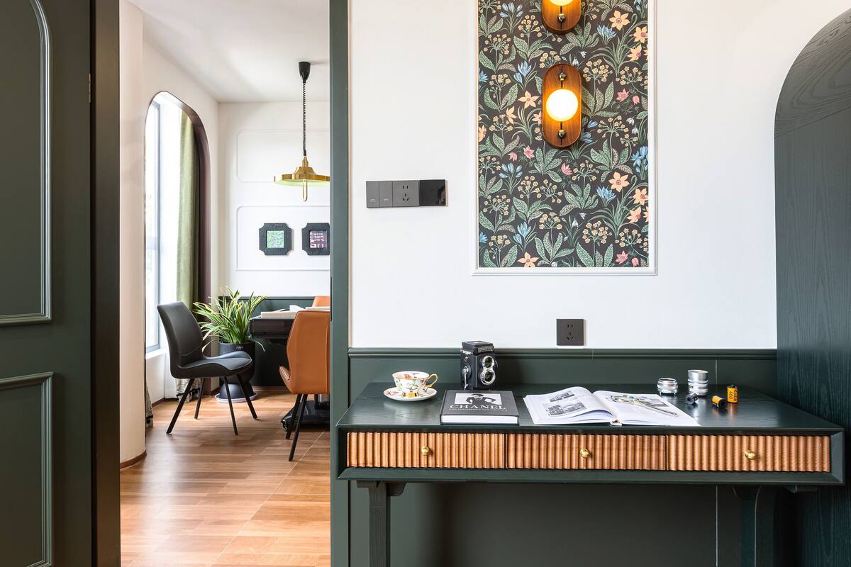 Una habitación moderna con un escritorio de madera, una planta en maceta y una lámpara fijada a la pared.