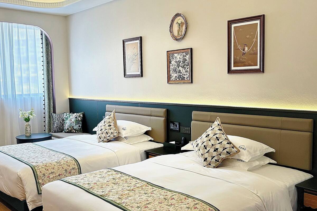 Habitación de hotel con dos camas, una mesita de noche y una ventana con cortinas.