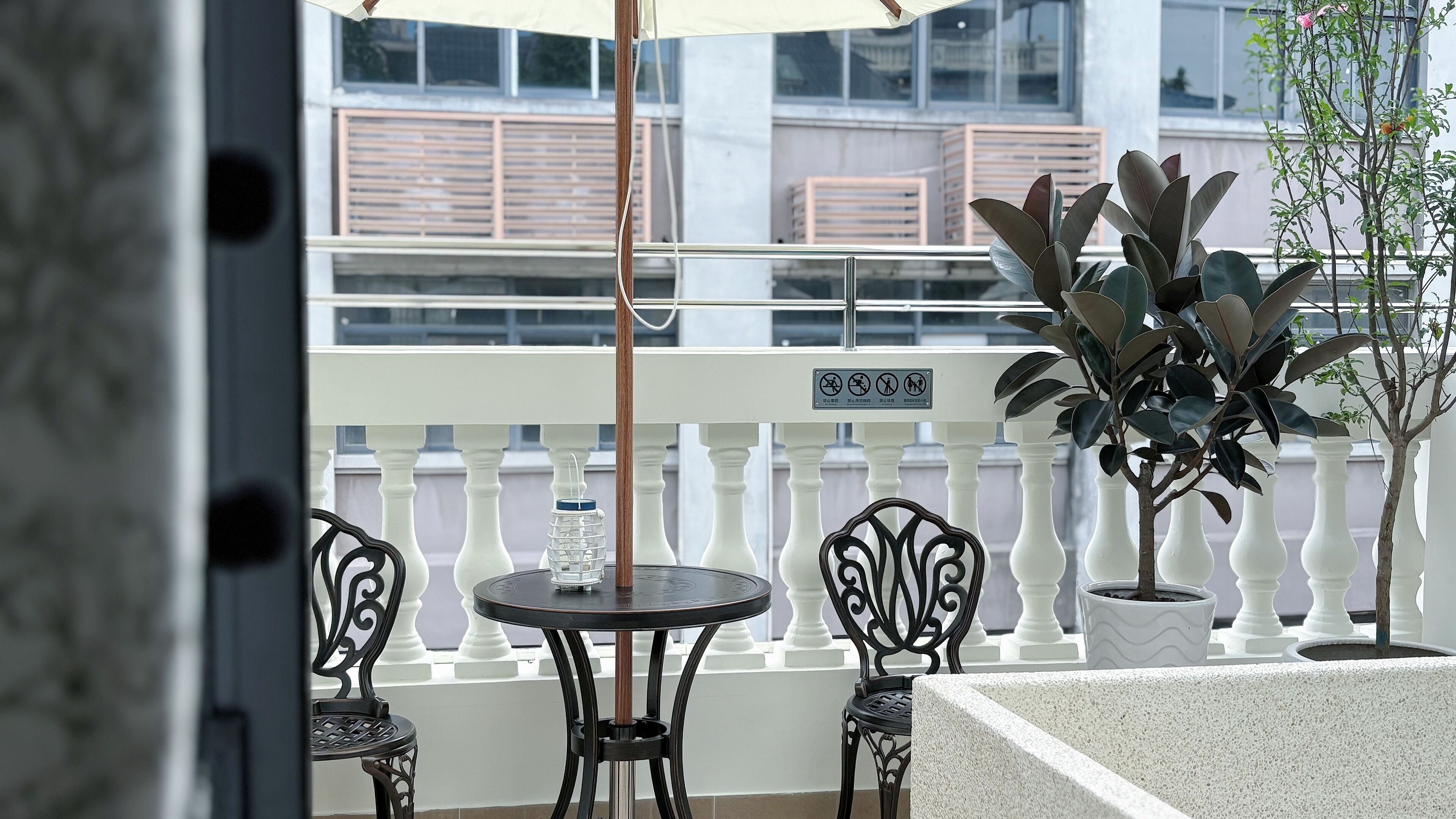 A balcony with a white railing, two round tables, and chairs, a potted plant, and a water bottle.