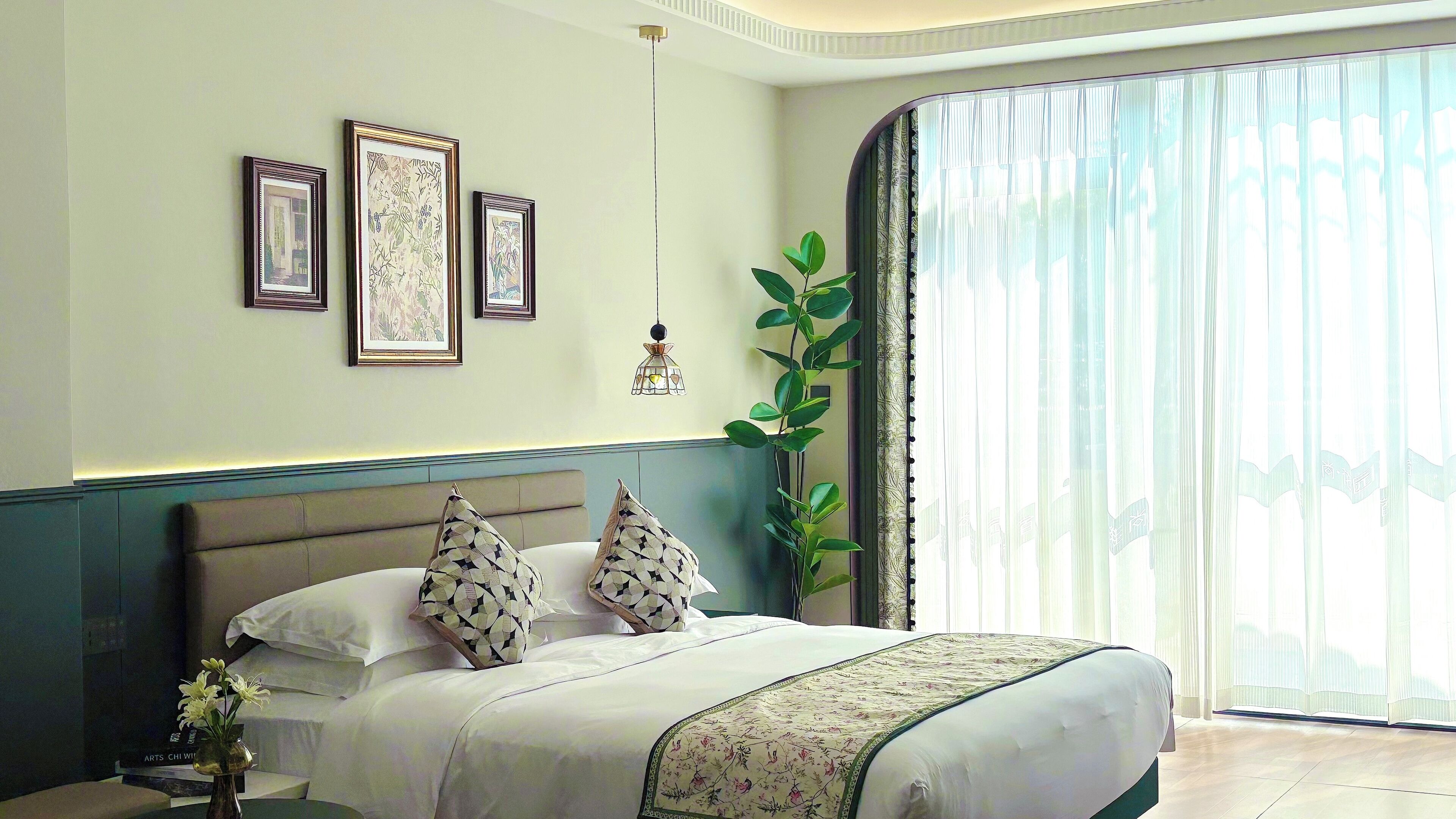 Un dormitorio con cama, mesita de noche, lámpara colgante y un gran ventanal con cortinas.