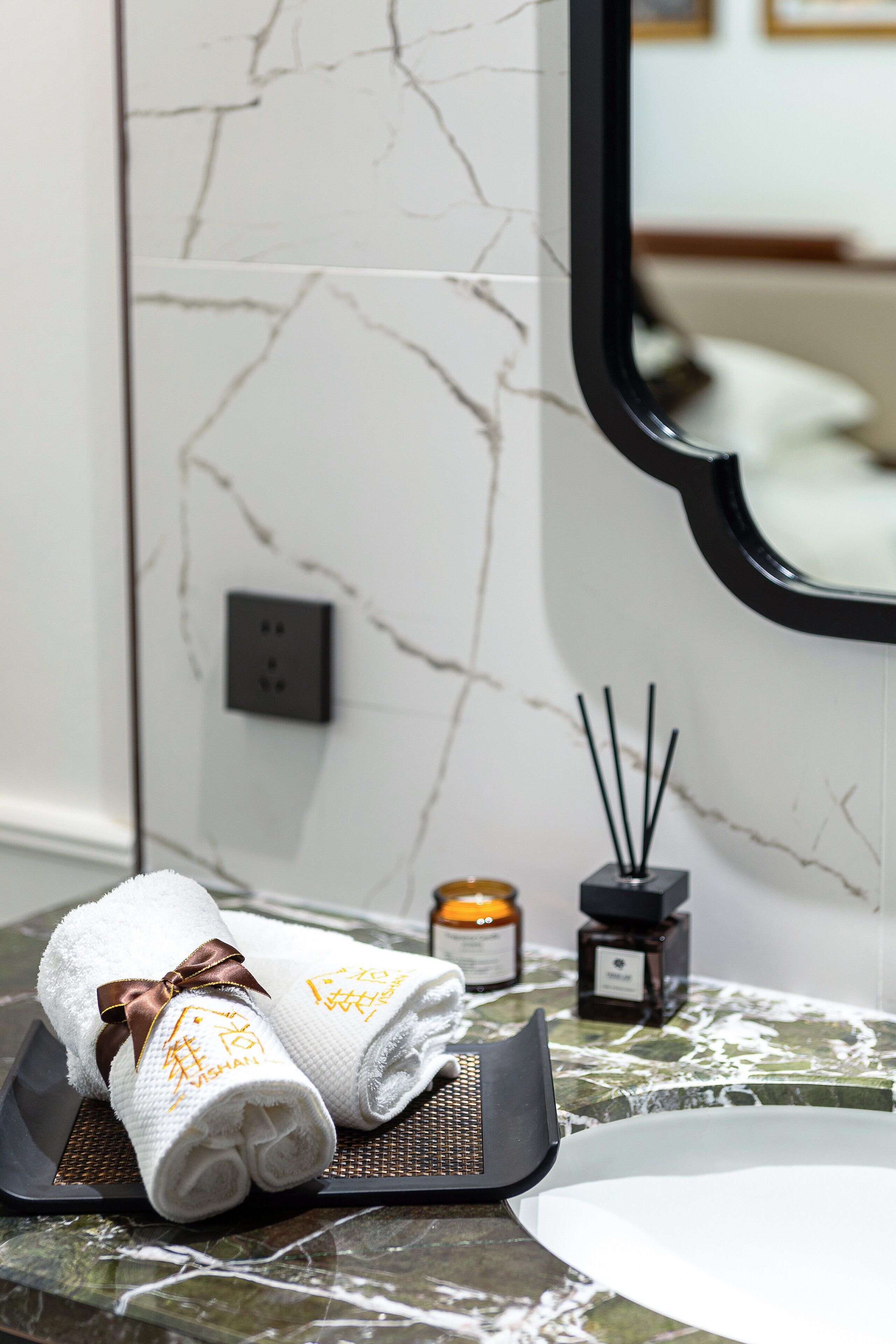A bathroom with a marble wall, a towel rack with folded towels, a candle, and a reed diffuser.