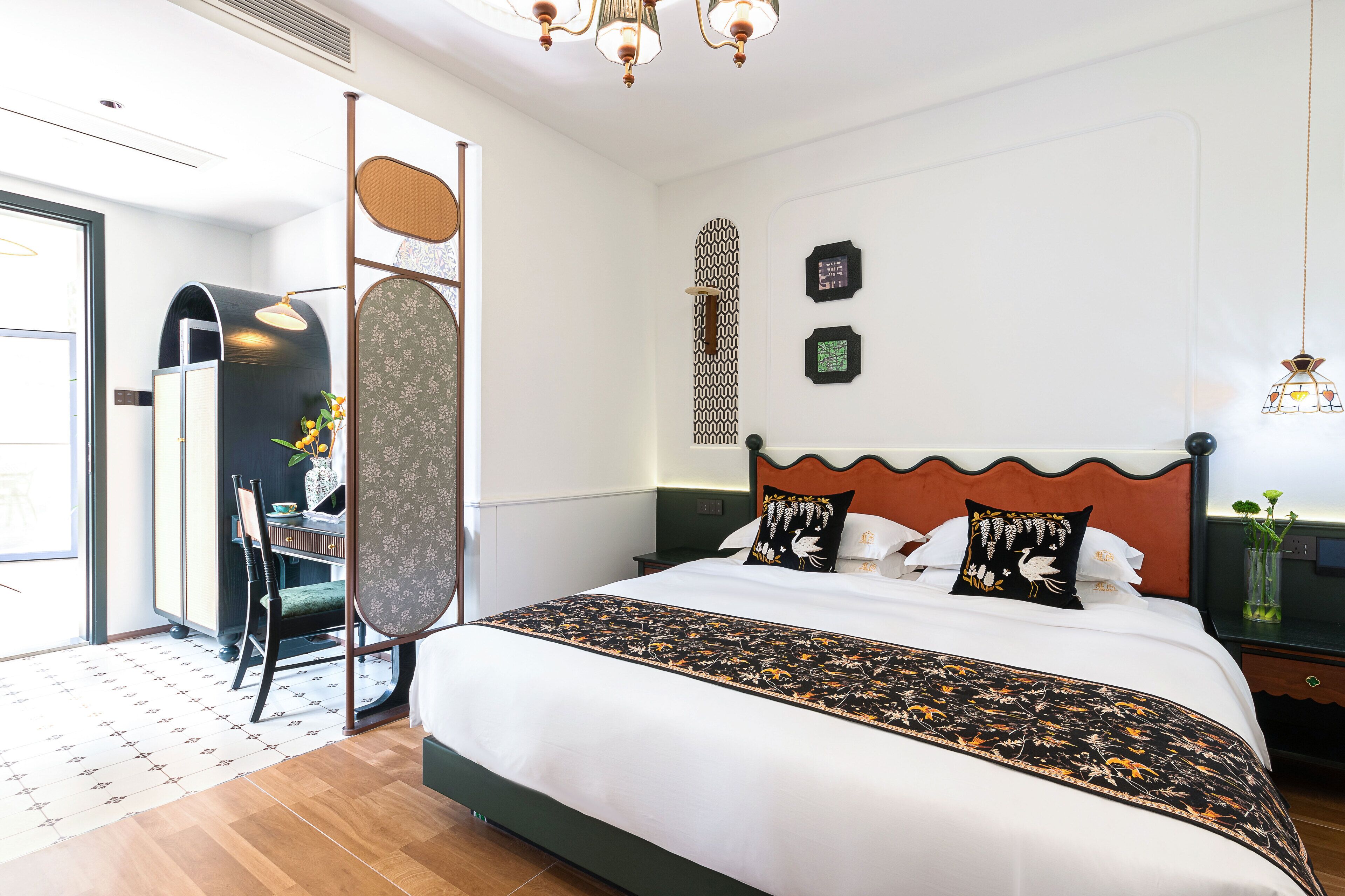 A neatly arranged bedroom with a large bed, a wooden chair, a small table, and a decorative wall panel.