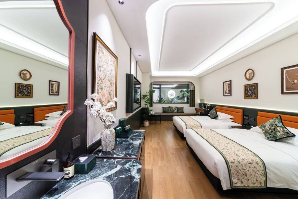 Habitación de hotel con dos camas, un espejo grande, una encimera de mármol y un pequeño rincón de descanso con vistas al exterior.