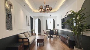 A modern living room with a sofa, dining table, and chairs. There is a TV mounted on the wall and a potted plant. - Vishan Garden Boutique Hotel (Xiamen)