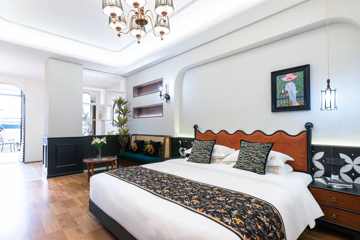 Habitación de hotel con una cama grande, una mesita con un florero, un sofá y vistas al exterior.