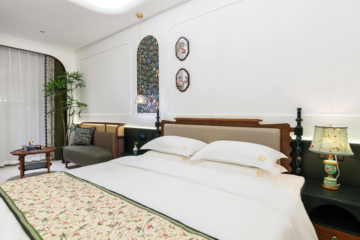 Habitación de hotel con una cama grande, una mesita de noche, una lámpara, una ventana con cortinas y un espejo montado en la pared.