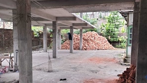 Un chantier de construction avec des piliers en béton apparent, un tas de briques et du matériel de construction.