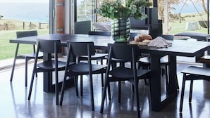 A modern dining area with a large table, chairs, pendant lighting, and a view of the ocean.