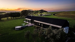 A modern farmhouse with a large open patio, surrounded by lush green fields and a sunset in the background.