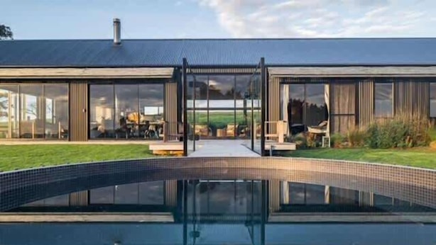 A modern house with a large glass facade, a swimming pool, and a well-maintained lawn.