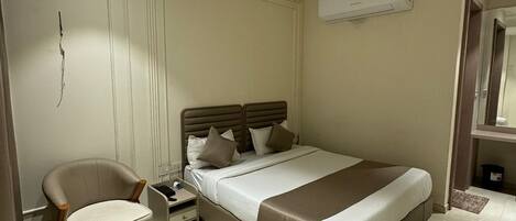A hotel room with a bed, a chair, a bedside table, and a round marble table.