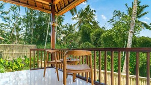 A wooden deck with a railing, surrounded by lush greenery and palm trees. - Villa Kuma Ubud (Tegallalang)