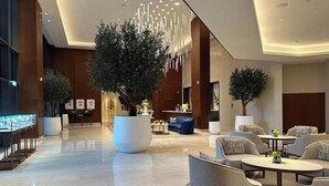 Un vestíbulo amplio con mobiliario moderno, un gran árbol central y una zona de bar.