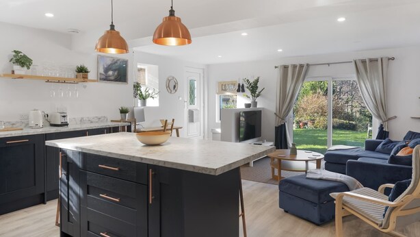 Een moderne keuken met een centraal eiland, hanglampen en een zithoek met een bank en poef.