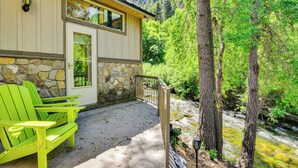 Une maison avec des fondations en pierre, une terrasse en bois et un fauteuil Adirondack vert.