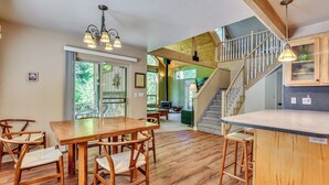 Un vaste espace de salle à manger avec une table et des chaises en bois, une cuisine dotée d’un comptoir-bar et un escalier menant à un niveau supérieur.