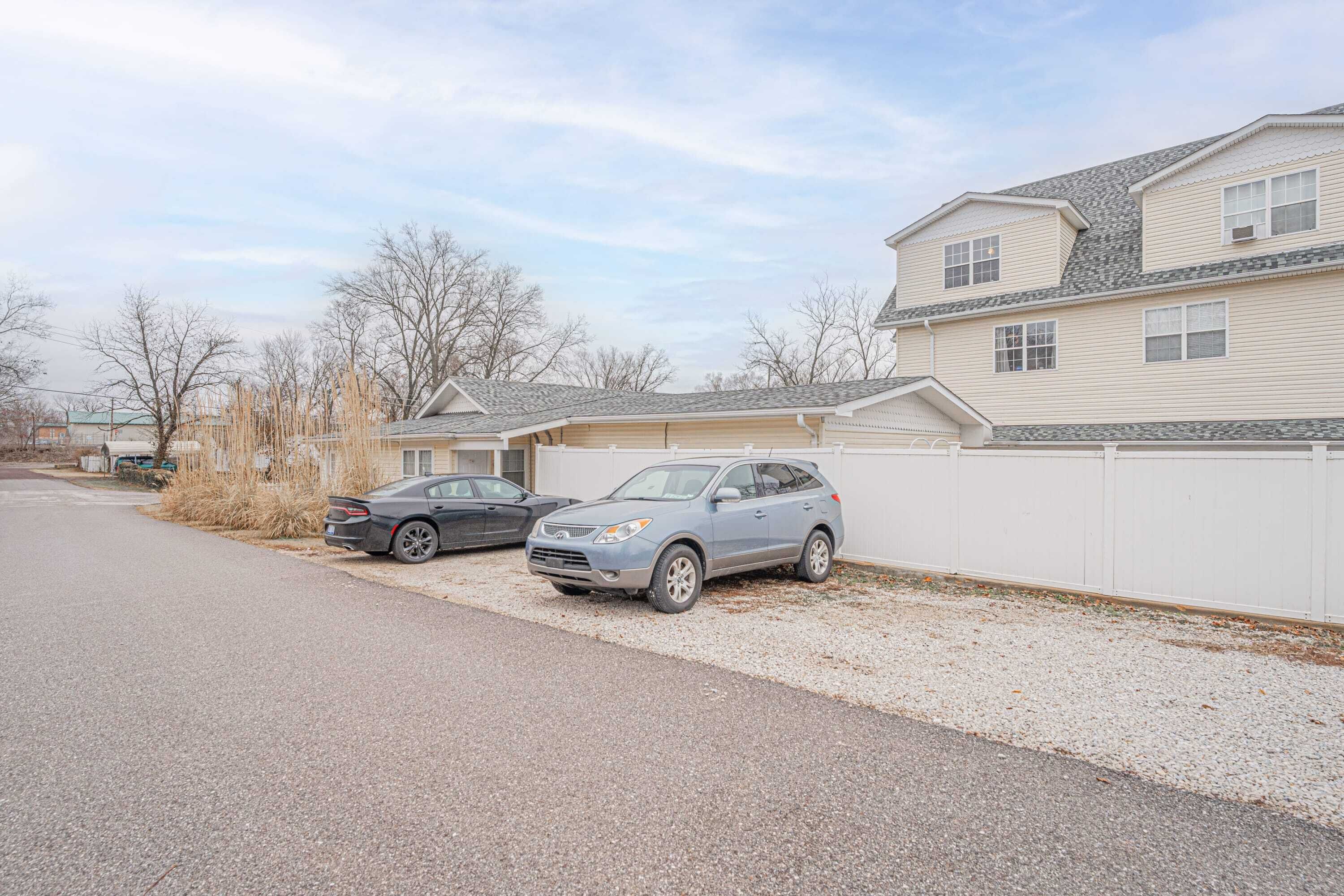 A residential area with two parked cars, a house with a white exterior, and a gravel driveway.