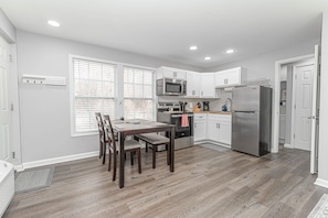 Una cocina moderna con armarios blancos, un refrigerador de acero inoxidable y un comedor con mesa y sillas de madera.