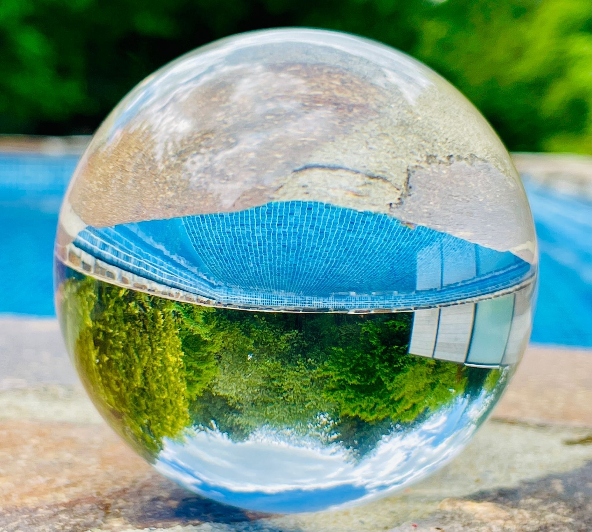 A clear glass sphere reflecting a building and greenery.