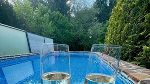 Deux verres contenant un liquide transparent sont posés sur une surface en pierre, près d’une piscine dont les carreaux sont bleus.