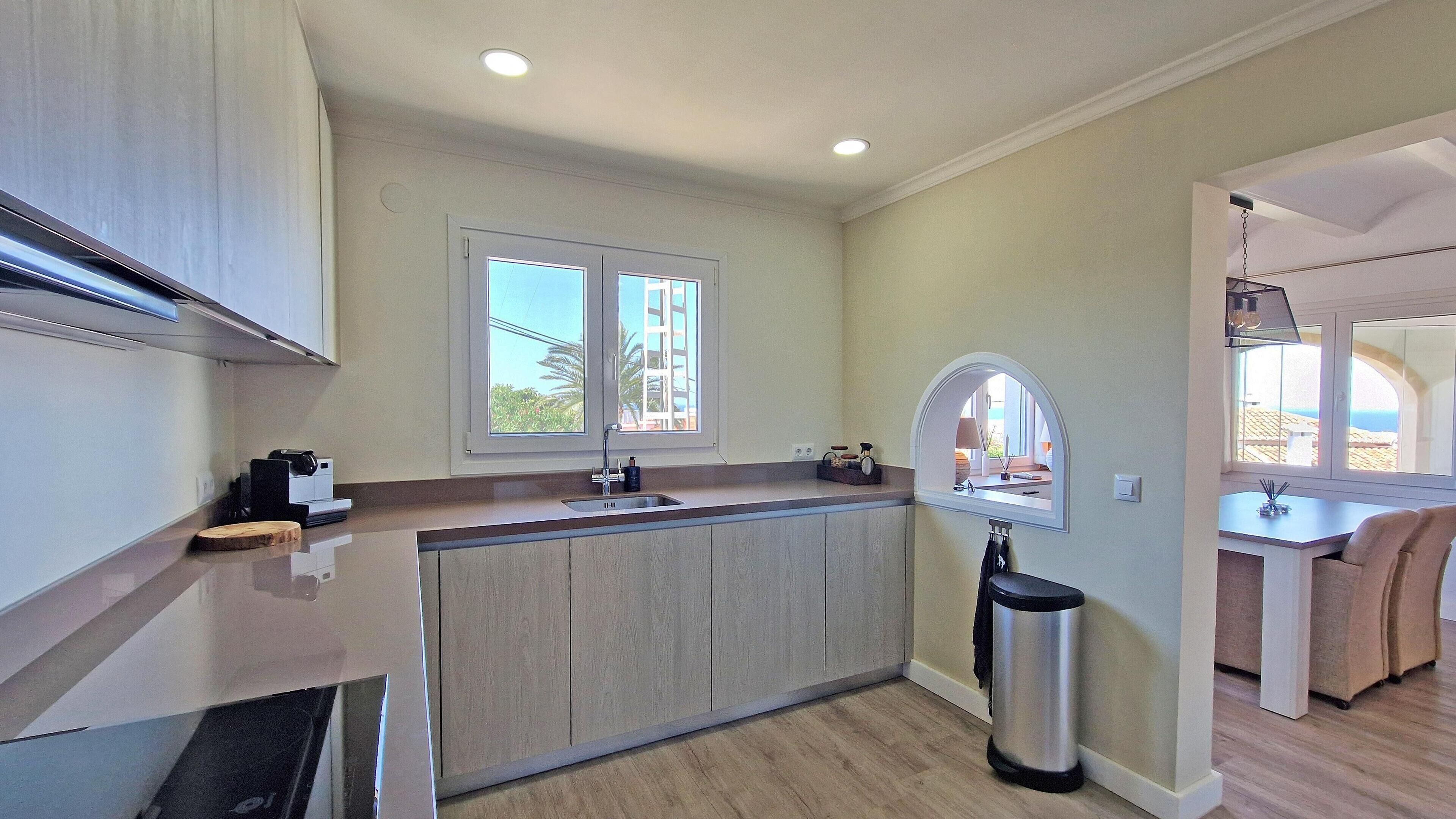 A modern kitchen with a central island, a window with a view, and a small trash bin.