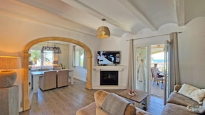 A spacious living area with a fireplace, a television mounted above it, and a balcony with a view of the ocean. - Casa Esmick - Denia, Costa Blanca (Denia)