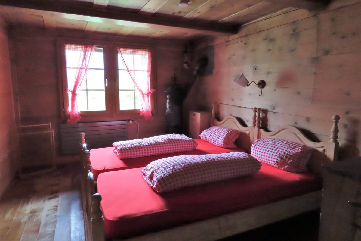 Habitación con dos camas, cabecero de madera, una ventana con cortinas y una lámpara fijada a la pared.