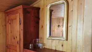 Ein Holzinnenraum einer Hütte mit einem Holzkabinett, einem Regal mit Gläsern und einem Spiegel.