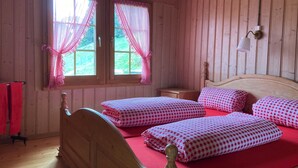 Ein Zimmer mit Holzboden, zwei Betten, roter Bettwäsche und einem Fenster mit Vorhängen.