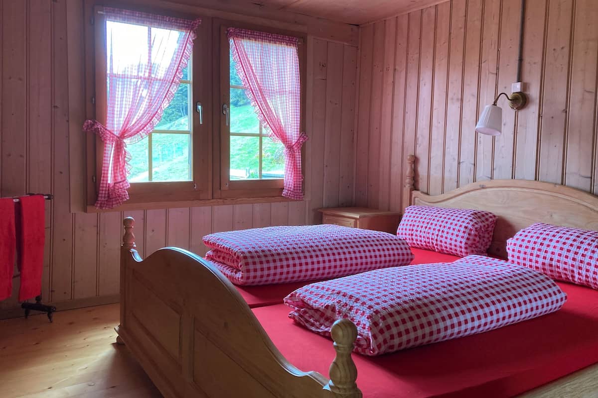 Una habitación de madera con dos camas, ropa de cama roja y una ventana con cortinas.