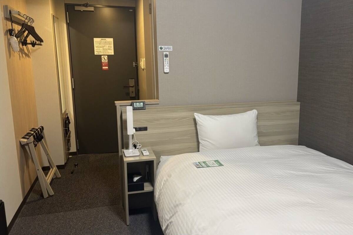 Una habitación de hotel con cama, mesita de noche, espejo, puerta y perchero.