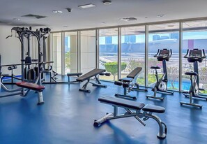 Une salle de sport équipée de matériel d’exercice, dotée de grandes fenêtres et d’un sol bleu.