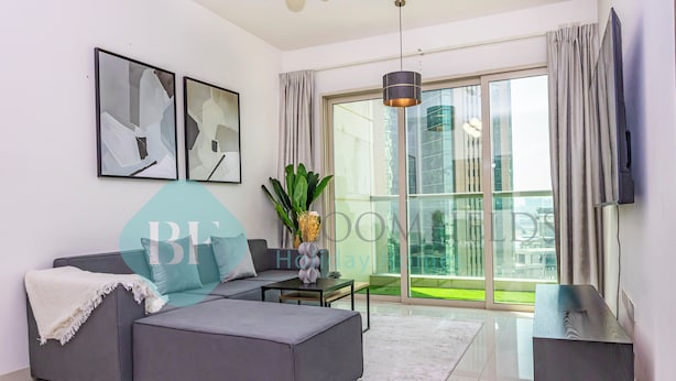 A modern living room with a grey sectional sofa, a small table, and a TV on a stand. - Bloomfeilds Royal 1Br Skyscraper (Abu Dhabi)