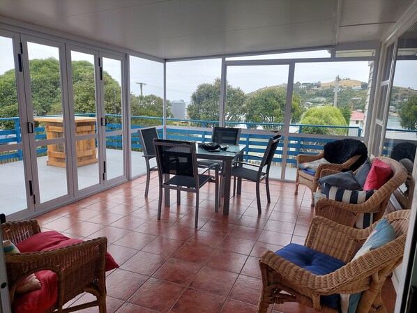 A sunlit balcony with a dining table, chairs, and wicker furniture. - Moeraki village, family sized house  stunning views, 50m to the beach. (Moeraki)