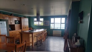 Eine geräumige Küche mit Holzschränken, einer zentralen Kochinsel mit Barhocker, einem Kühlschrank und einem großen Fenster für natürliches Licht.