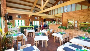 A restaurant with wooden interior, multiple tables set with white tablecloths and green napkins, and a bar area with a counter and stools. - Cozy Glamping Tent in Ardennes (Manhay)