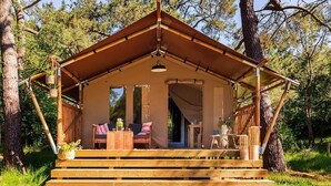A wooden cabin with a pitched roof, a porch with seating, and a door leading inside. - Cozy Glamping Tent in Ardennes (Manhay)