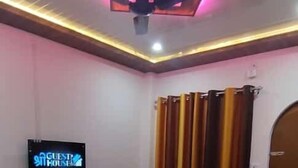 A bedroom with a bed, a flat-screen TV mounted on the wall, and a ceiling light fixture. - Shree Guest House (Varanasi)
