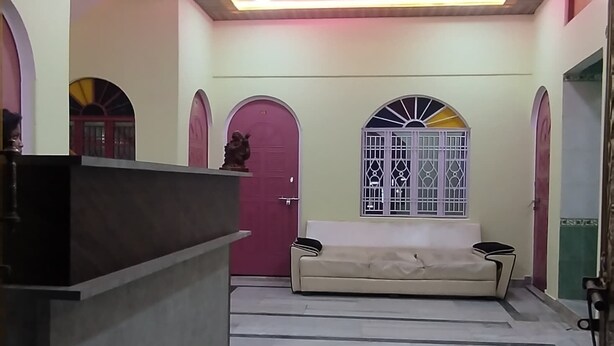 A reception area with a ceiling fan, a reception desk, a sofa, and a window with decorative bars. - Shree Guest House (Varanasi)