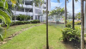 Un bâtiment moderne doté de balcons, entouré d’une pelouse bien entretenue et de palmiers.