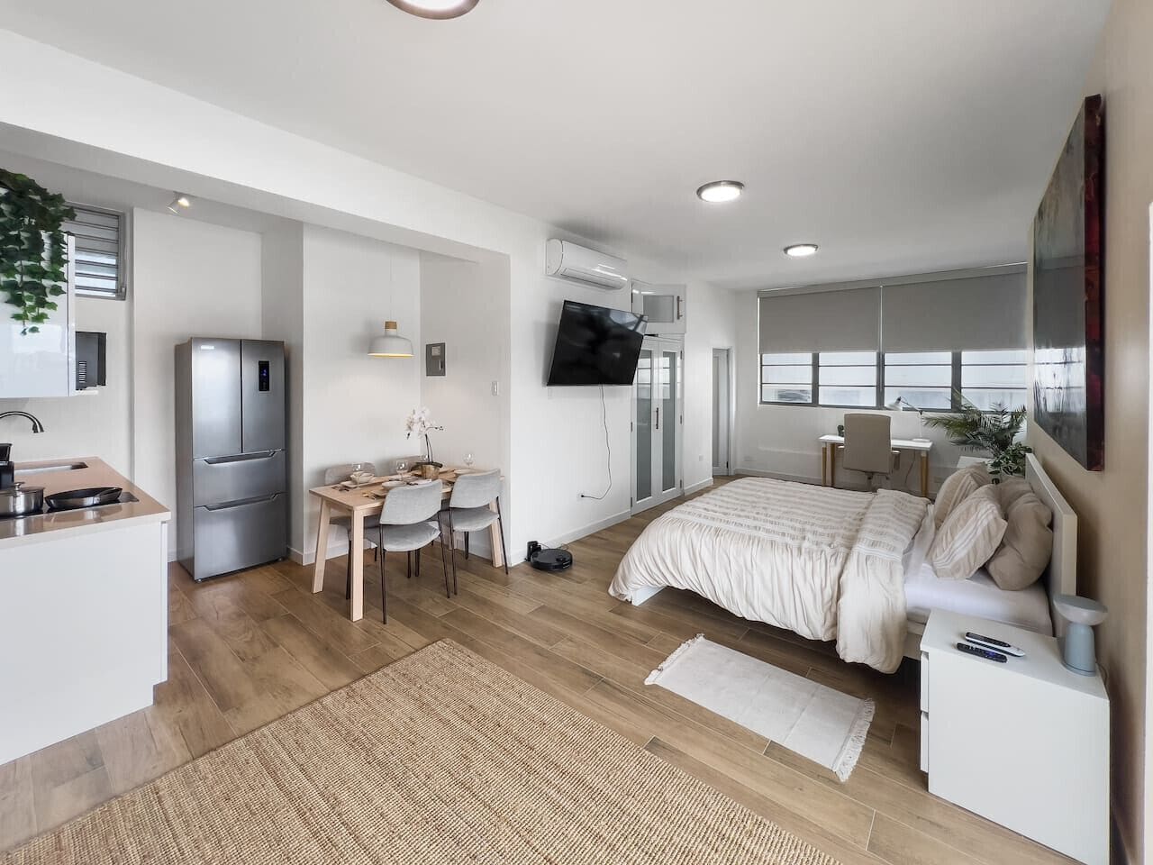 Ein modernes, kompaktes Wohnzimmer mit Küchenzeile, Essbereich, Schlafzimmer mit großem Bett und Wand-Fernseher.