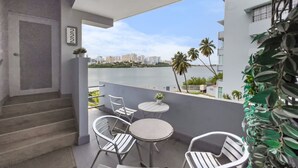 A balcony with white metal chairs and tables, a view of the city skyline, and a palm tree. - La Rada 222 | Studio Apt in San Juan With Views (San Juan)