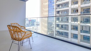 A balcony with two wicker chairs, a glass railing, and a view of a modern building with multiple floors. - Bloomfields Stylish 1Br Binghatti Creek (Dubai)