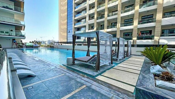 A modern hotel with a swimming pool, outdoor seating, and a large building in the background. - Bloomfields Stylish 1Br Binghatti Creek (Dubai)