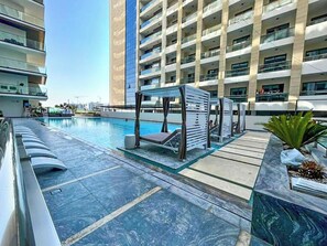 A modern hotel with a swimming pool, outdoor seating, and a large building in the background. - Bloomfields Stylish 1Br Binghatti Creek (Dubai)