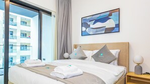 A neatly made bed with towels, a headboard, and a bedside table with a lamp. - Bloomfields Stylish 1Br Binghatti Creek (Dubai)
