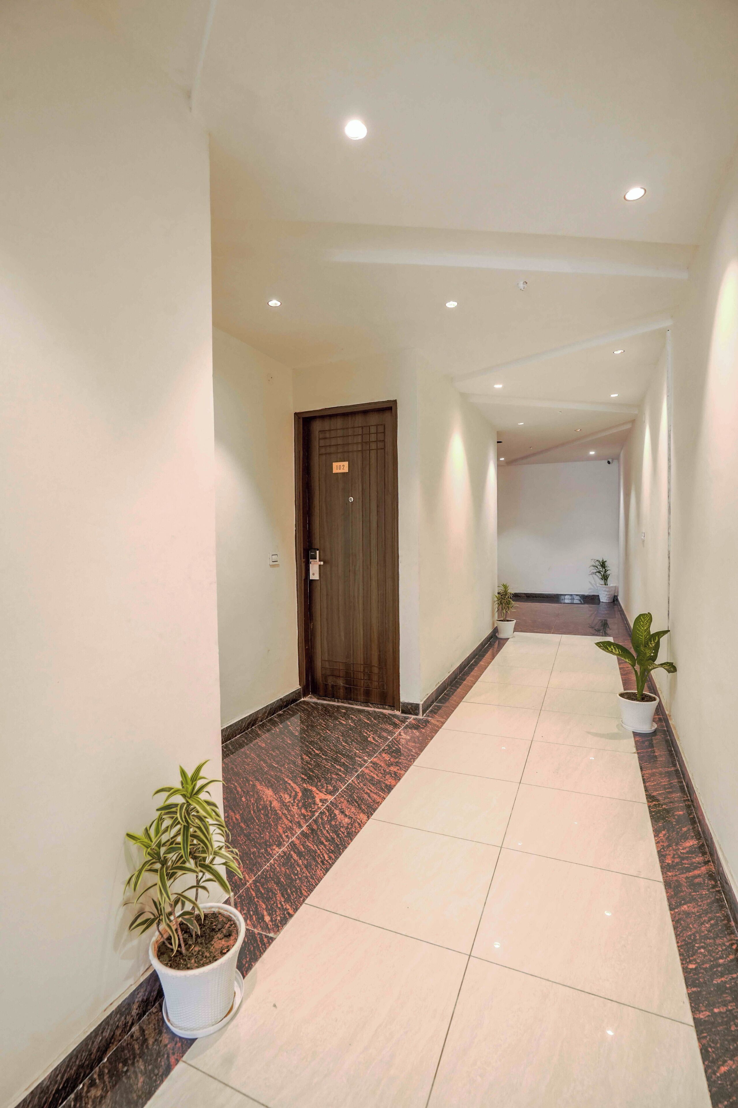 A hallway with a wooden door, potted plants, and tiled flooring.