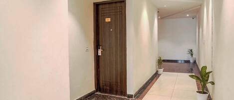 A hallway with a wooden door, potted plants, and tiled flooring.